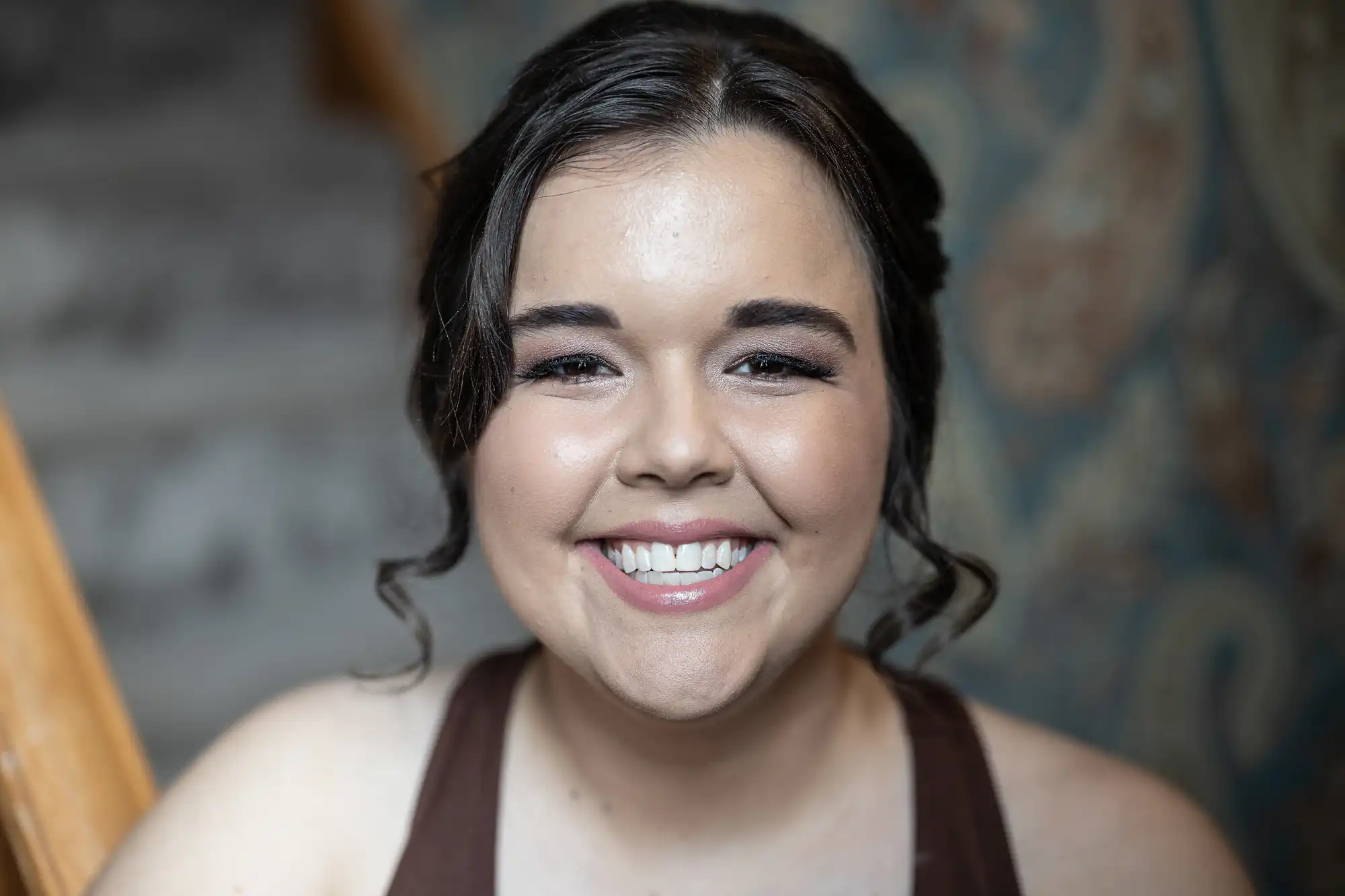 A woman with dark hair and a light complexion smiles at the camera. She is wearing a dark top and has a blurred background behind her.