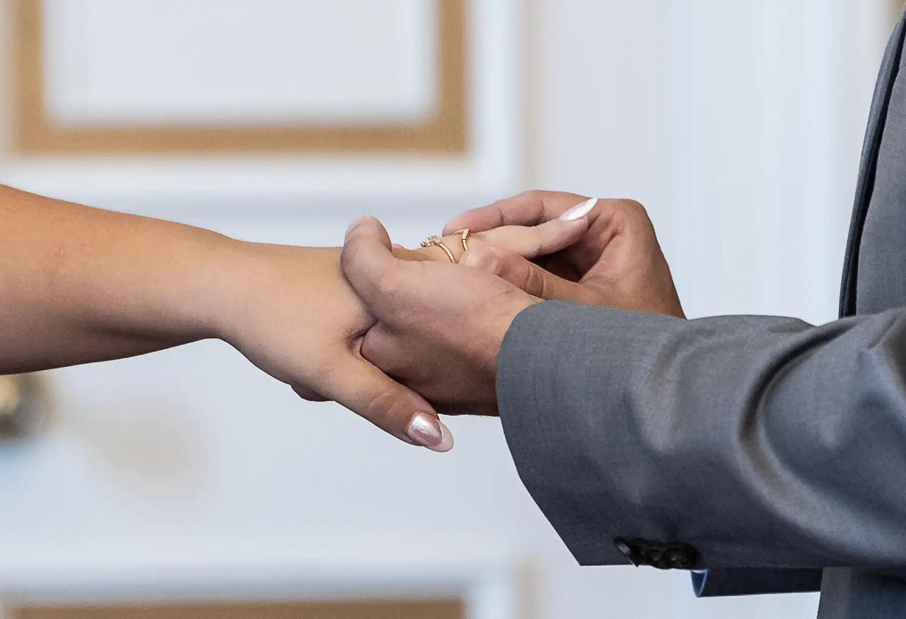 A person in a suit places a ring on another person's finger during a ceremony.