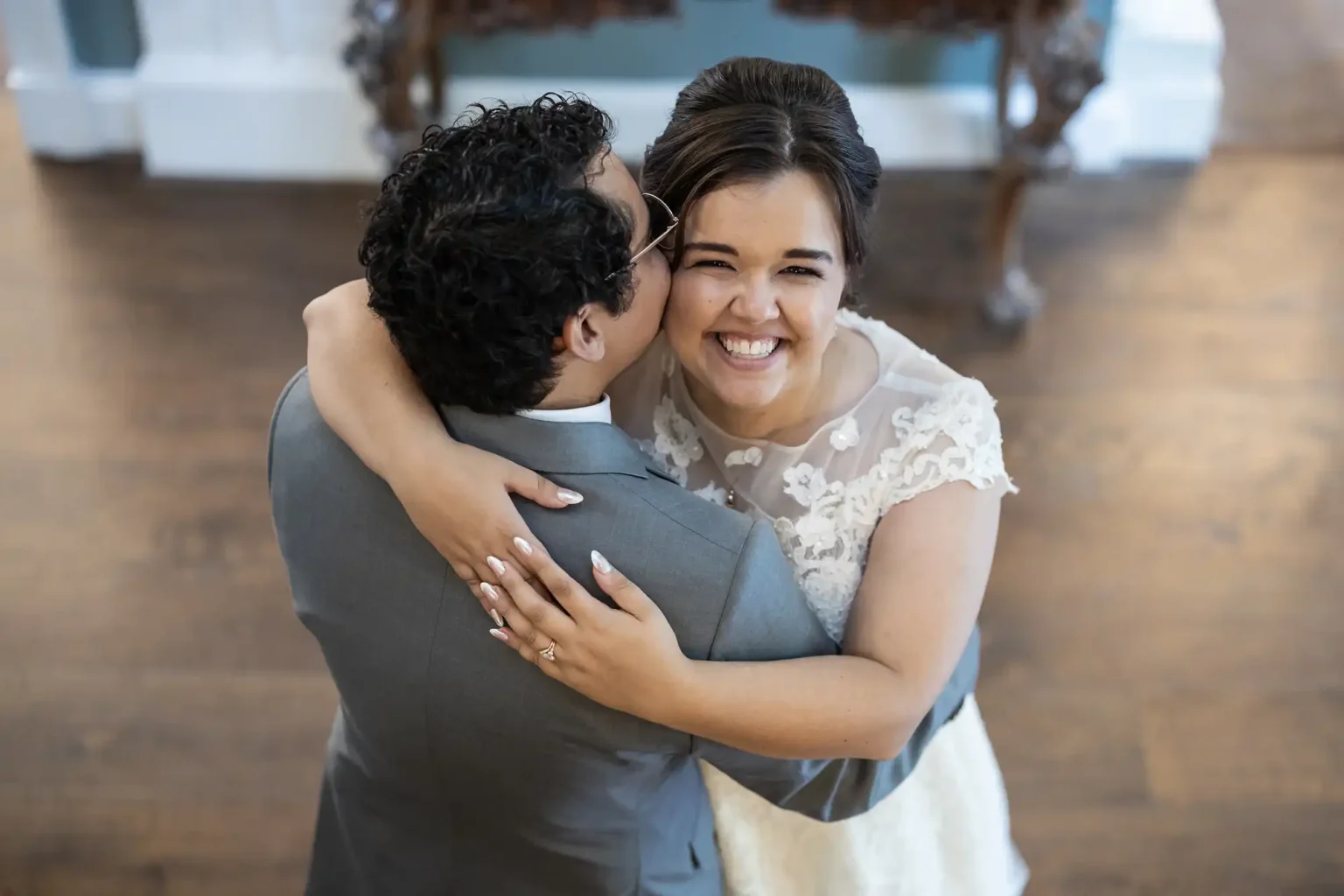 A couple embraces while dancing, viewed from above. The woman smiles brightly, and the man wears glasses and a grey suit.