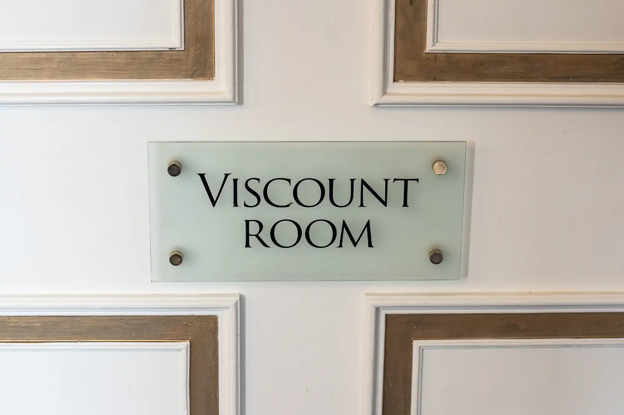 A sign on a wall reads "Viscount Room" in black text on a light background, bordered by a brass frame.