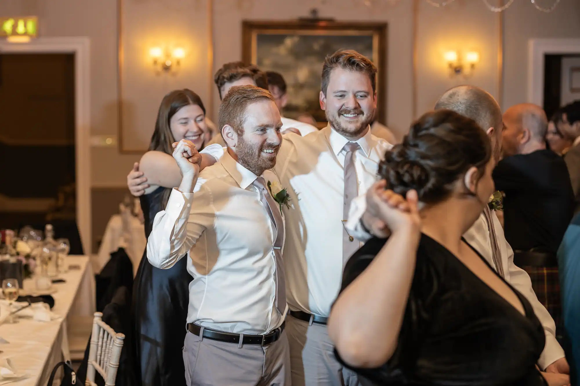 Group of people dressed formally are standing in a line with their arms linked, smiling and celebrating in a banquet hall.