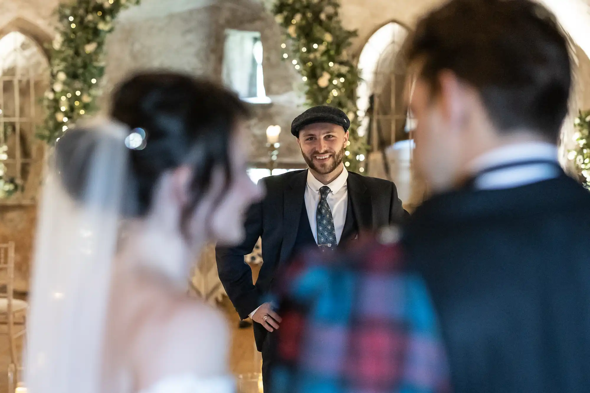 A man in a suit smiles at a bride and groom in a decorated indoor setting.