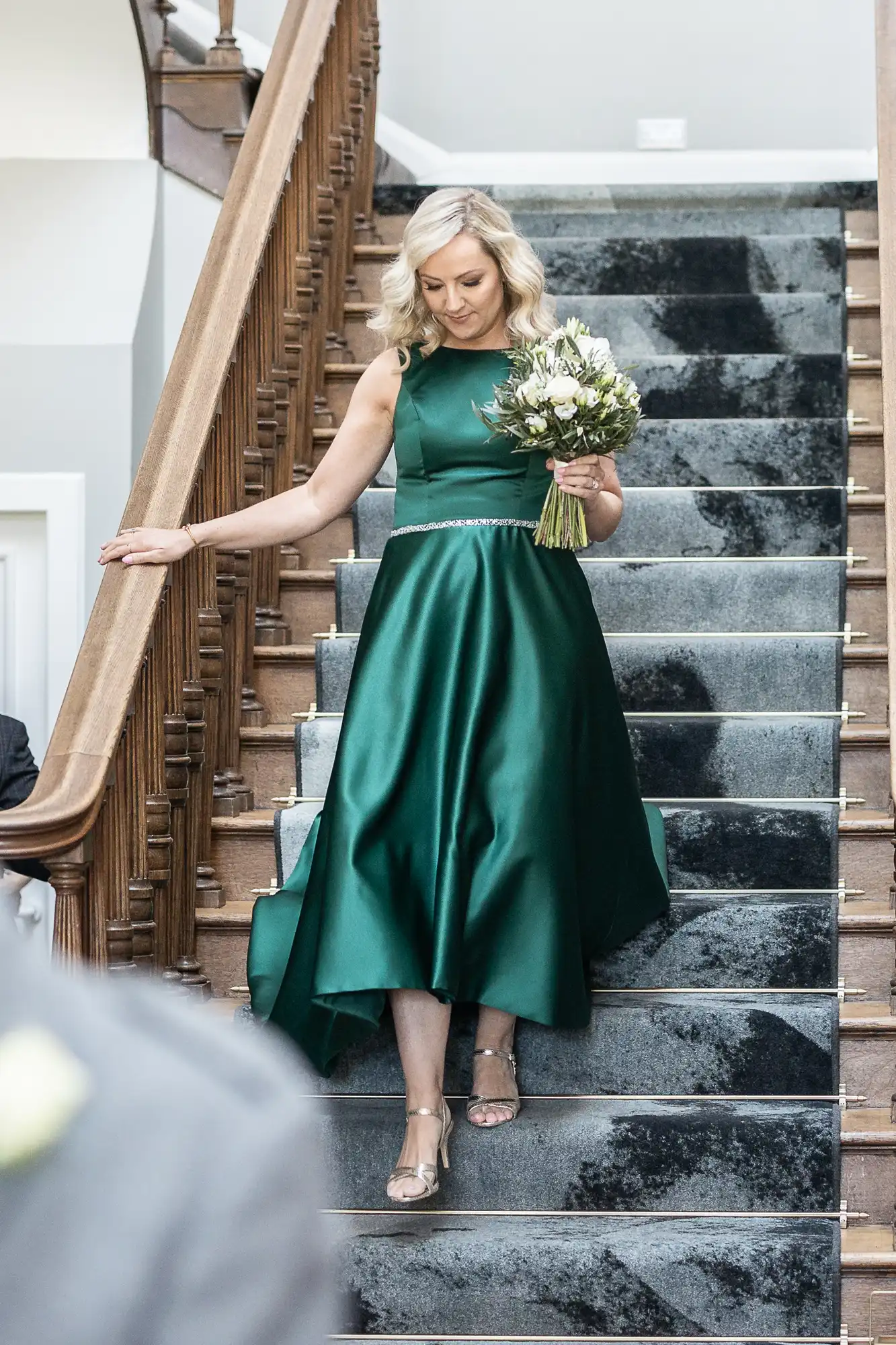 A woman in a green dress is descending a staircase while holding a bouquet of flowers.