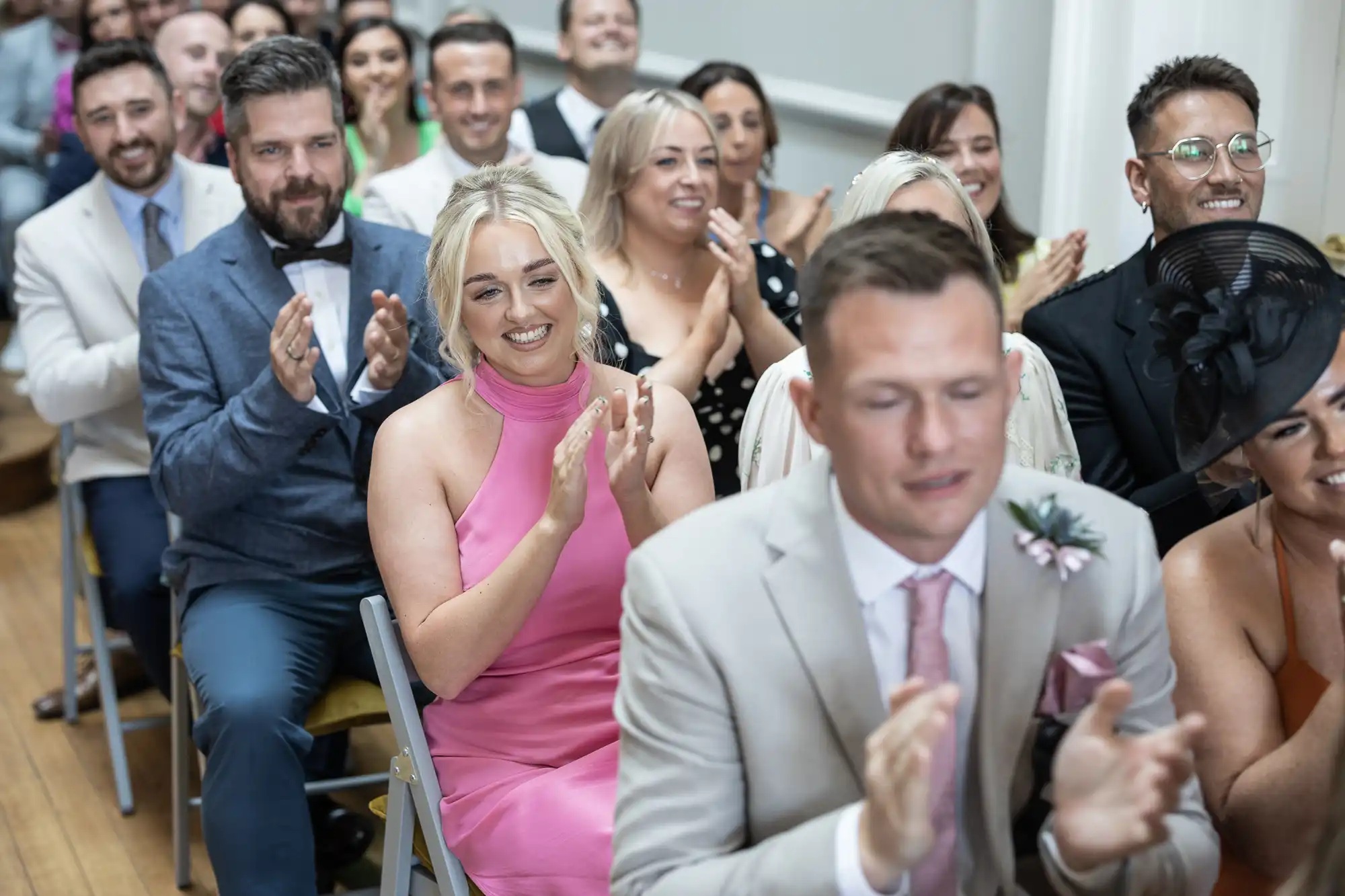 A group of people sit and clap, dressed formally, facing forward in what appears to be a celebratory or formal event.