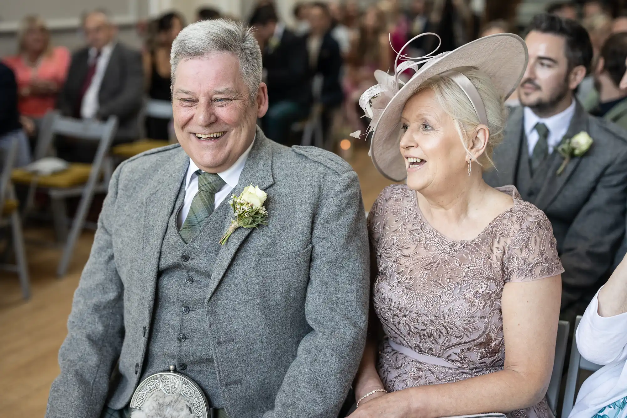 A man and woman, dressed in formal wear, are seated together at an event. Both are smiling and appear engaged with the proceedings.