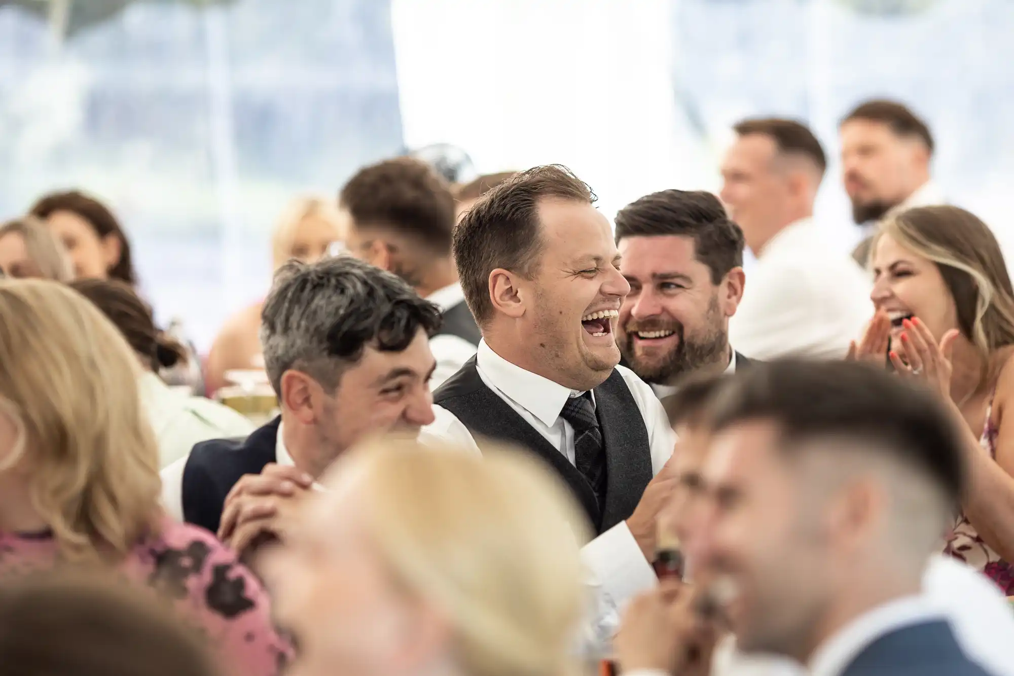 A group of people, dressed in formal attire, share a moment of laughter in a well-lit, crowded setting.