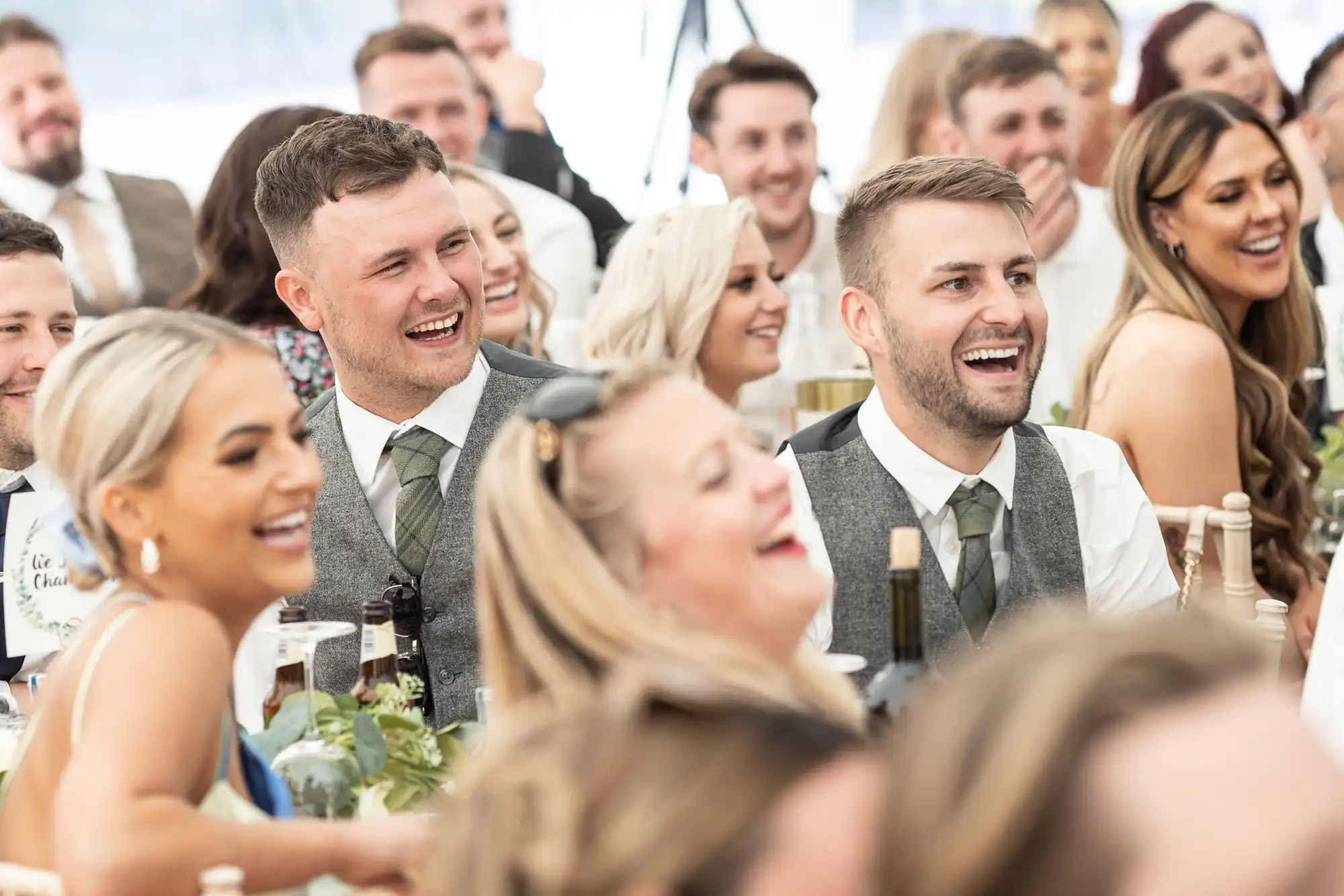 A group of people dressed in formal attire, seated at tables, smiling and laughing at an event.