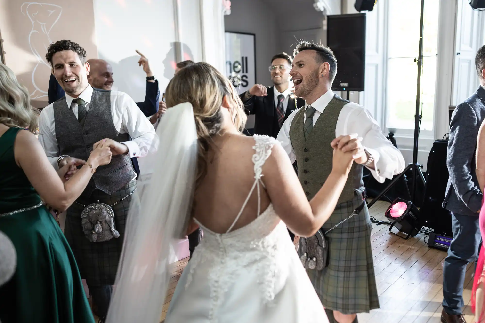 Bride and groom dance at a wedding reception, surrounded by guests in formal attire and traditional Scottish kilts.