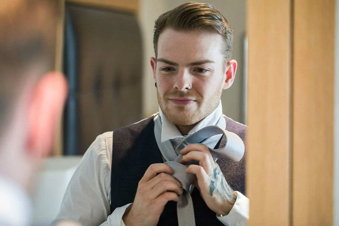 groom putting his tie on in front of mirror