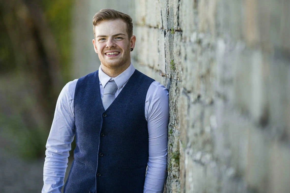 groom smiling leaning against stone wall