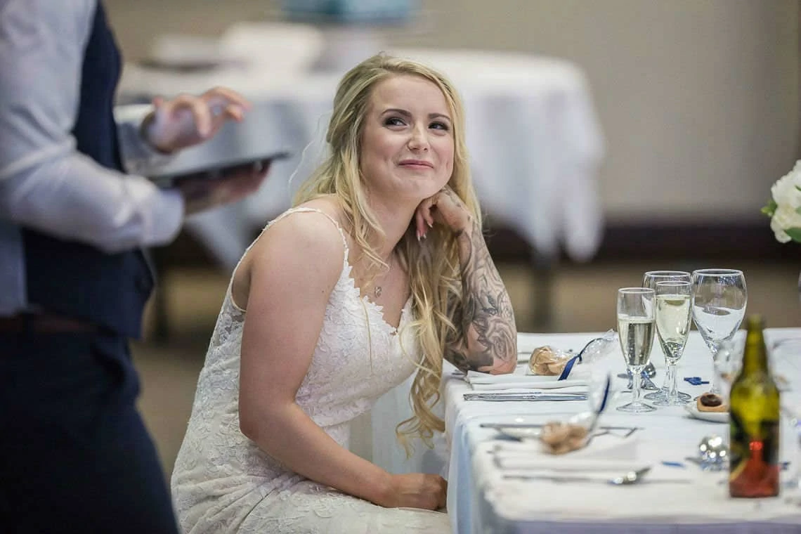 bride smiling as she watches groom doing his wedding speech