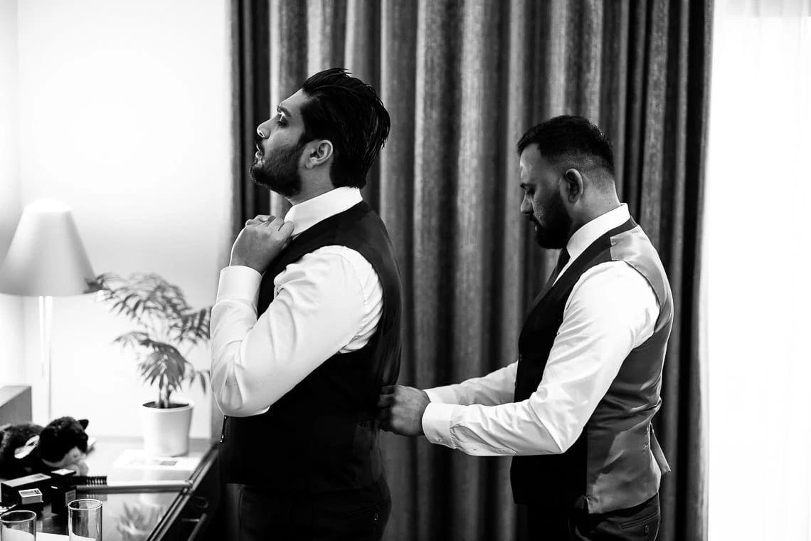 groomsman helps groom put on a waistcoat