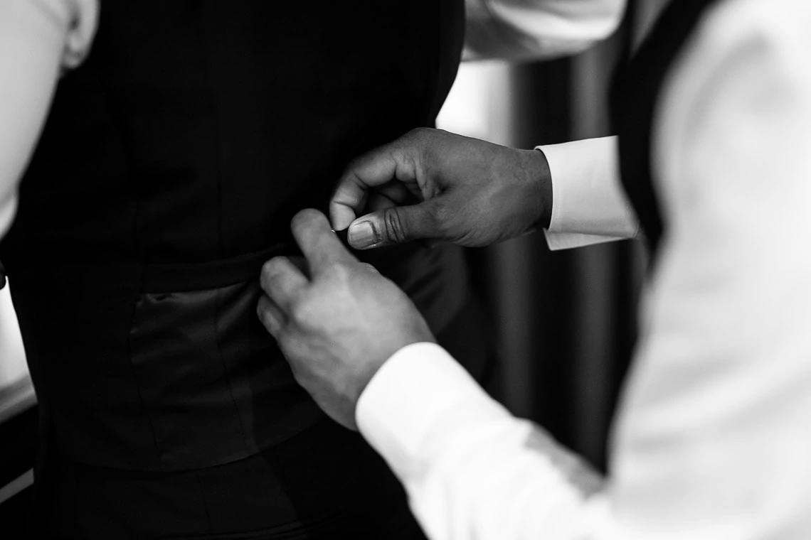 groomsman helps groom put on a waistcoat
