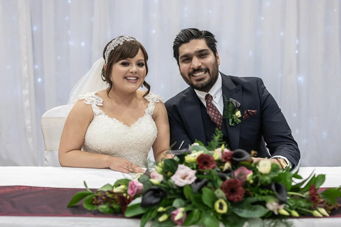 newlyweds smile at the camera while signing the marriage schedule