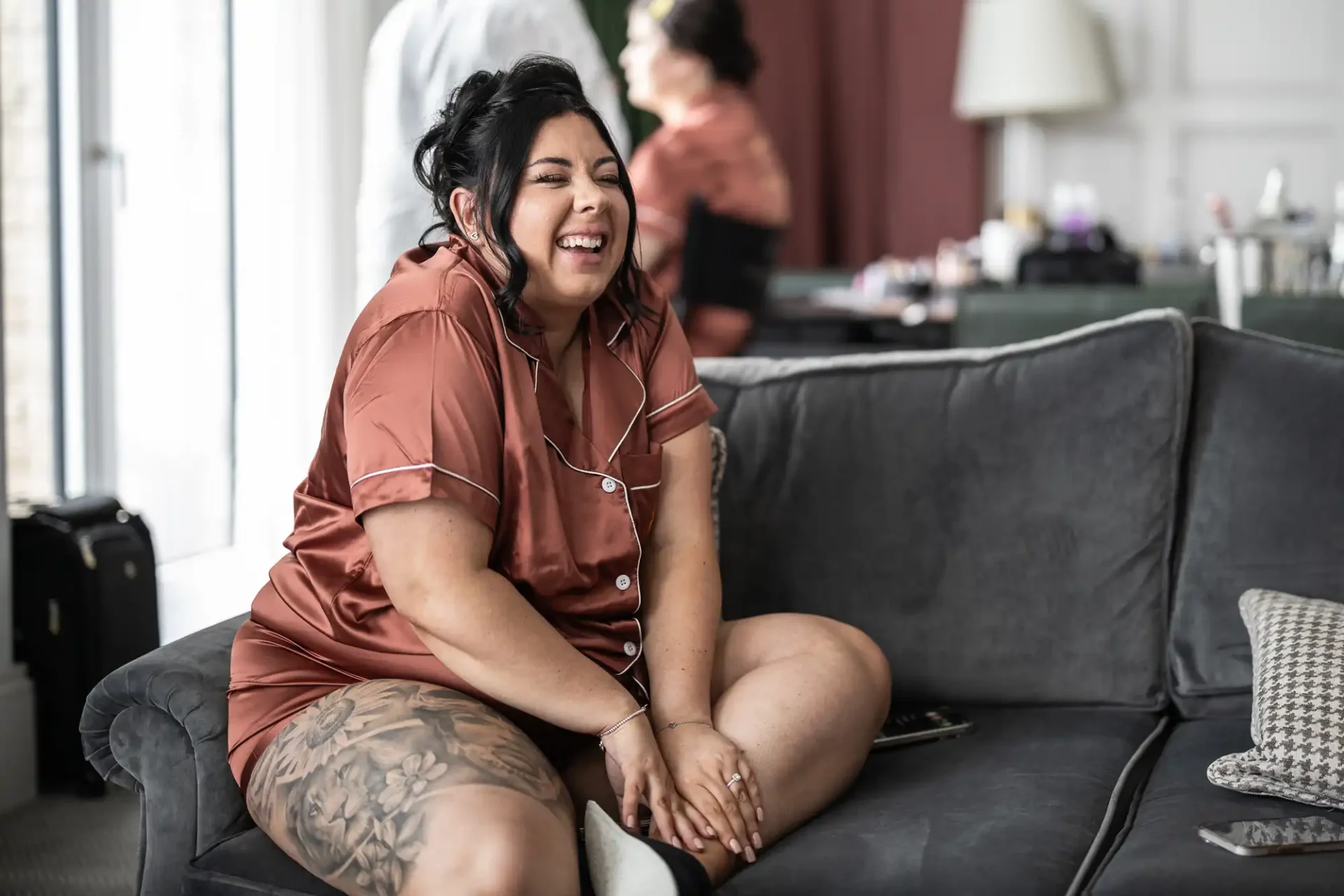 Person sitting on a couch, smiling and wearing satin pajamas.