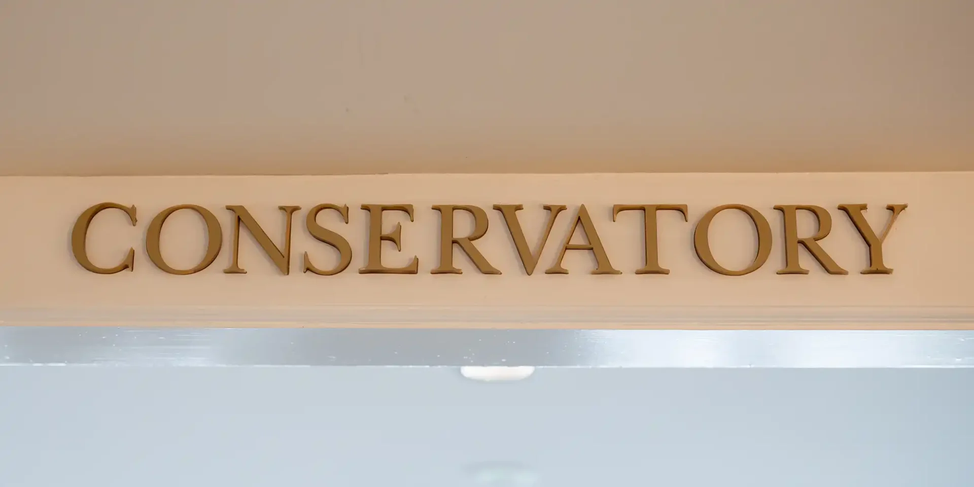 Brass letters spelling "CONSERVATORY" are mounted on a light beige wall above a doorway.