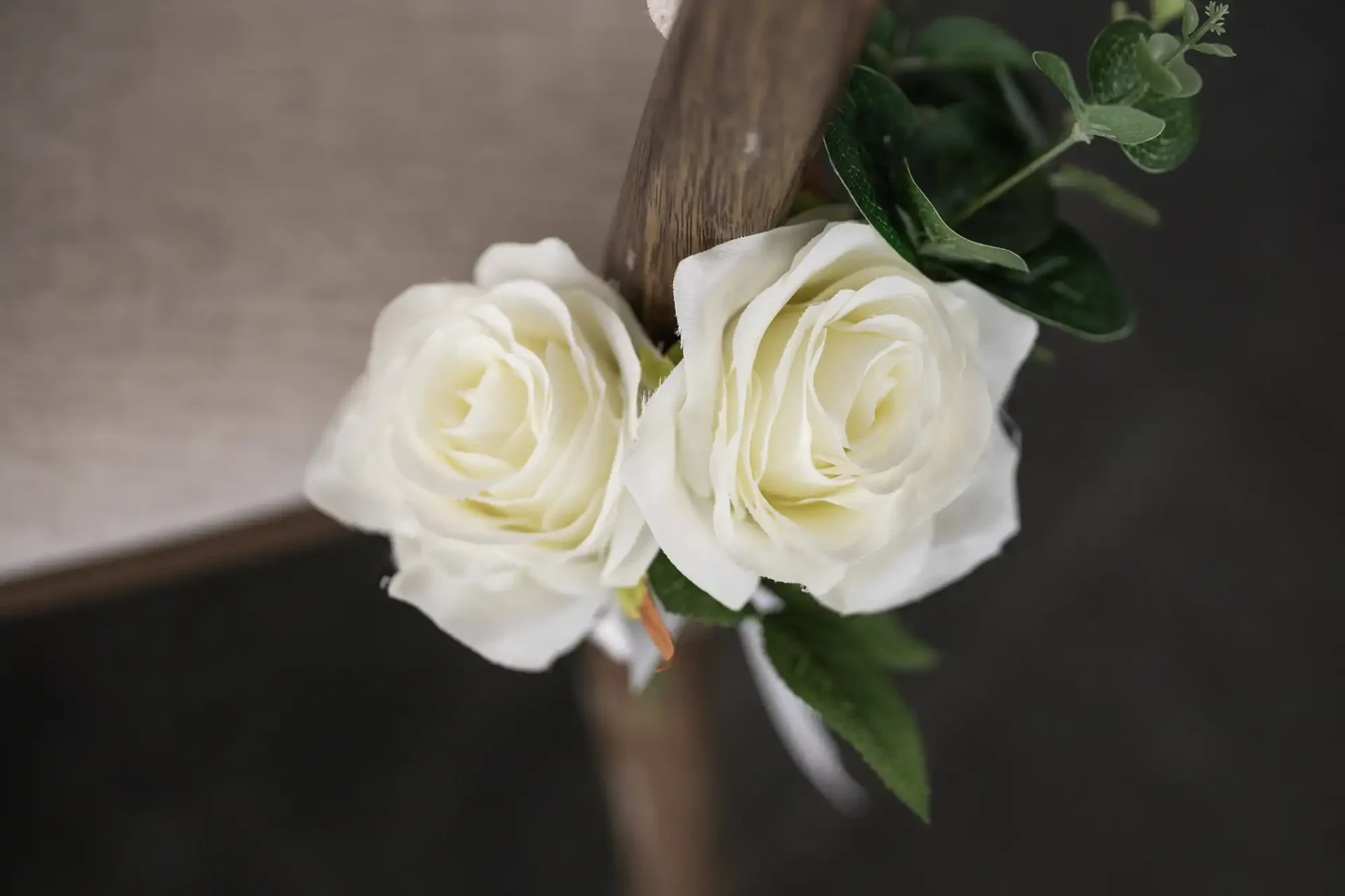 Two white roses with green leaves attached to a wooden chair.