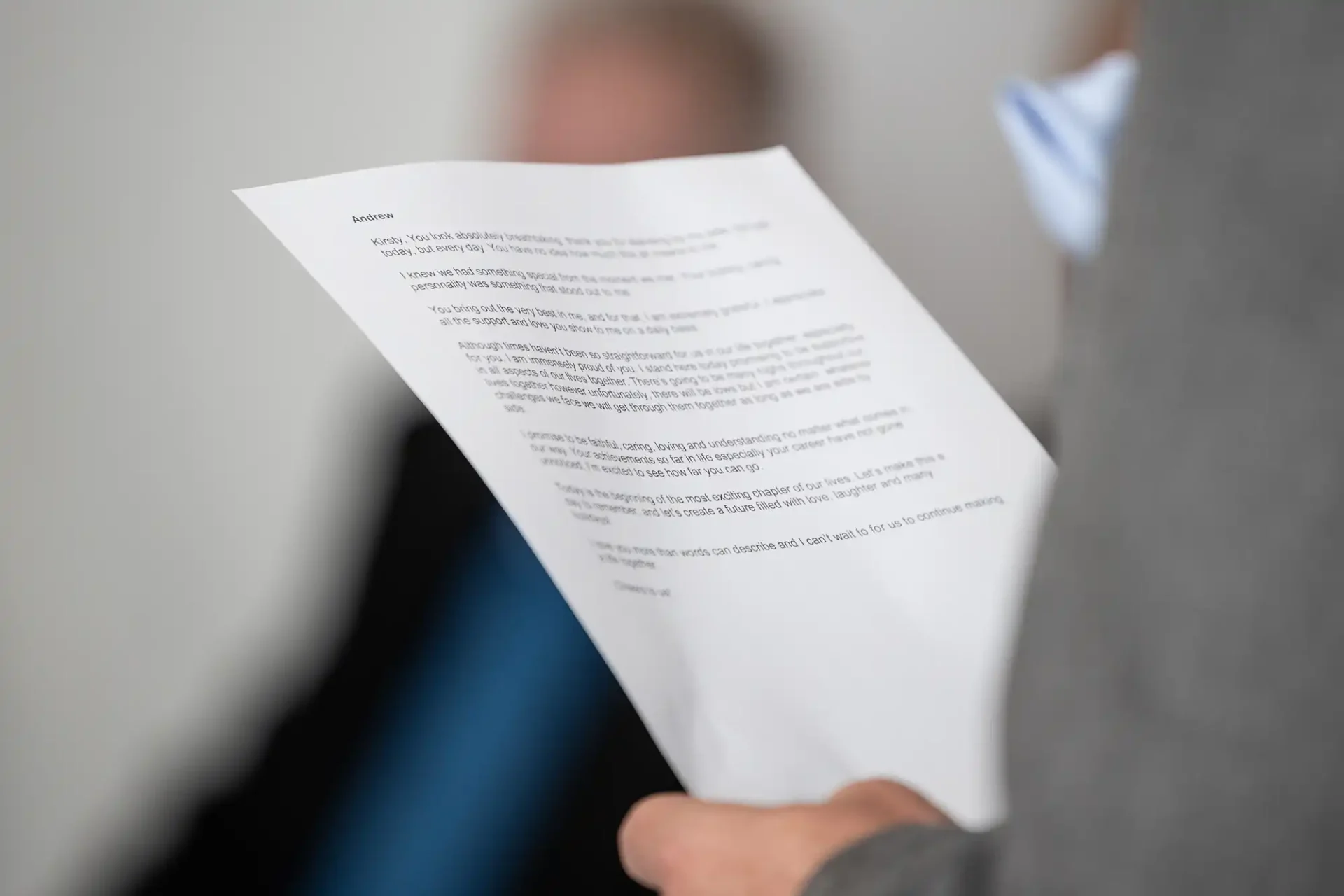 Close-up of a person holding a printed document in one hand, with another figure blurred in the background.