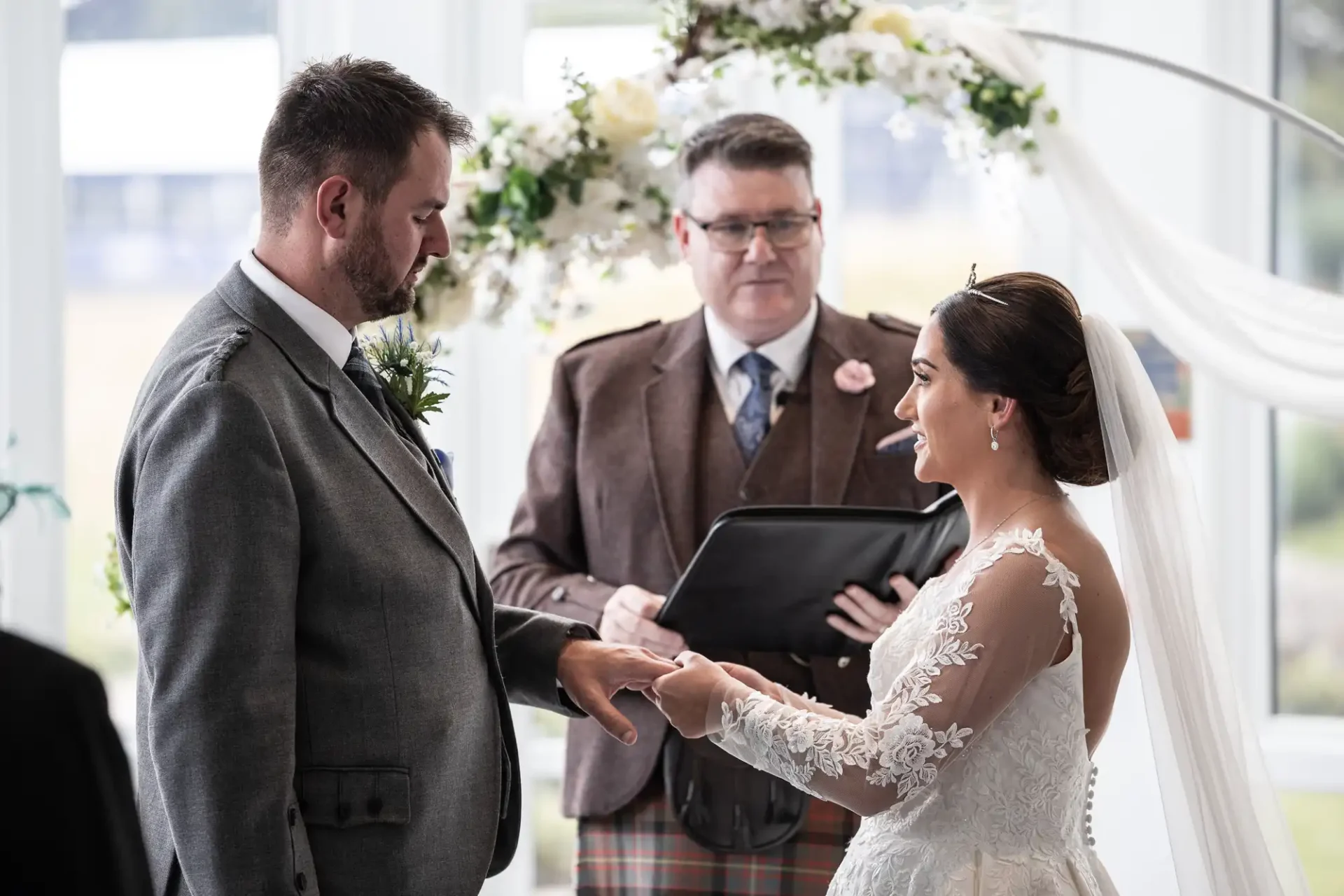 A bride and groom exchange vows at their wedding ceremony, with an officiant standing behind them.