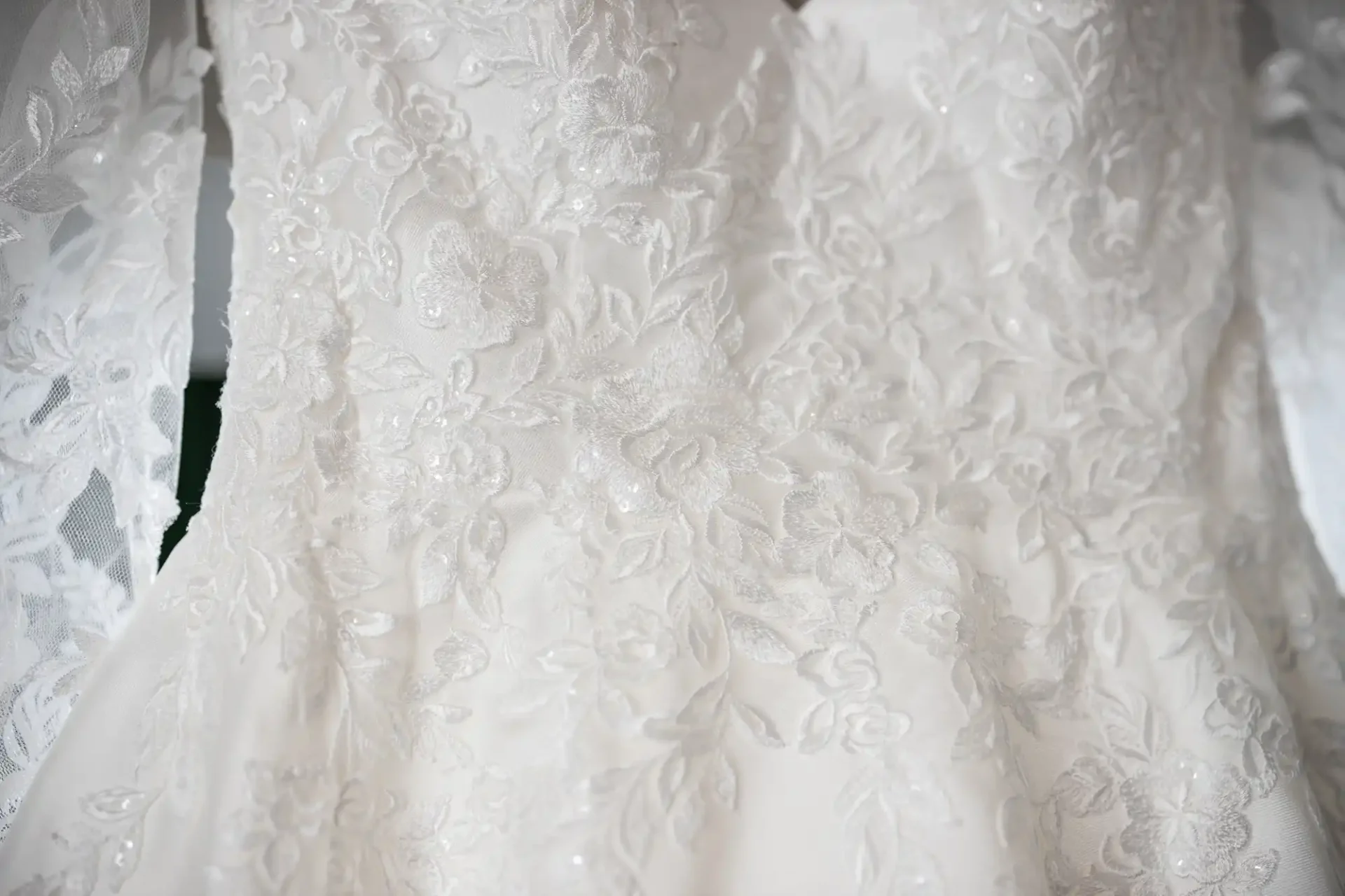 Close-up of intricate white lace on a wedding dress, featuring floral patterns and delicate detailing.