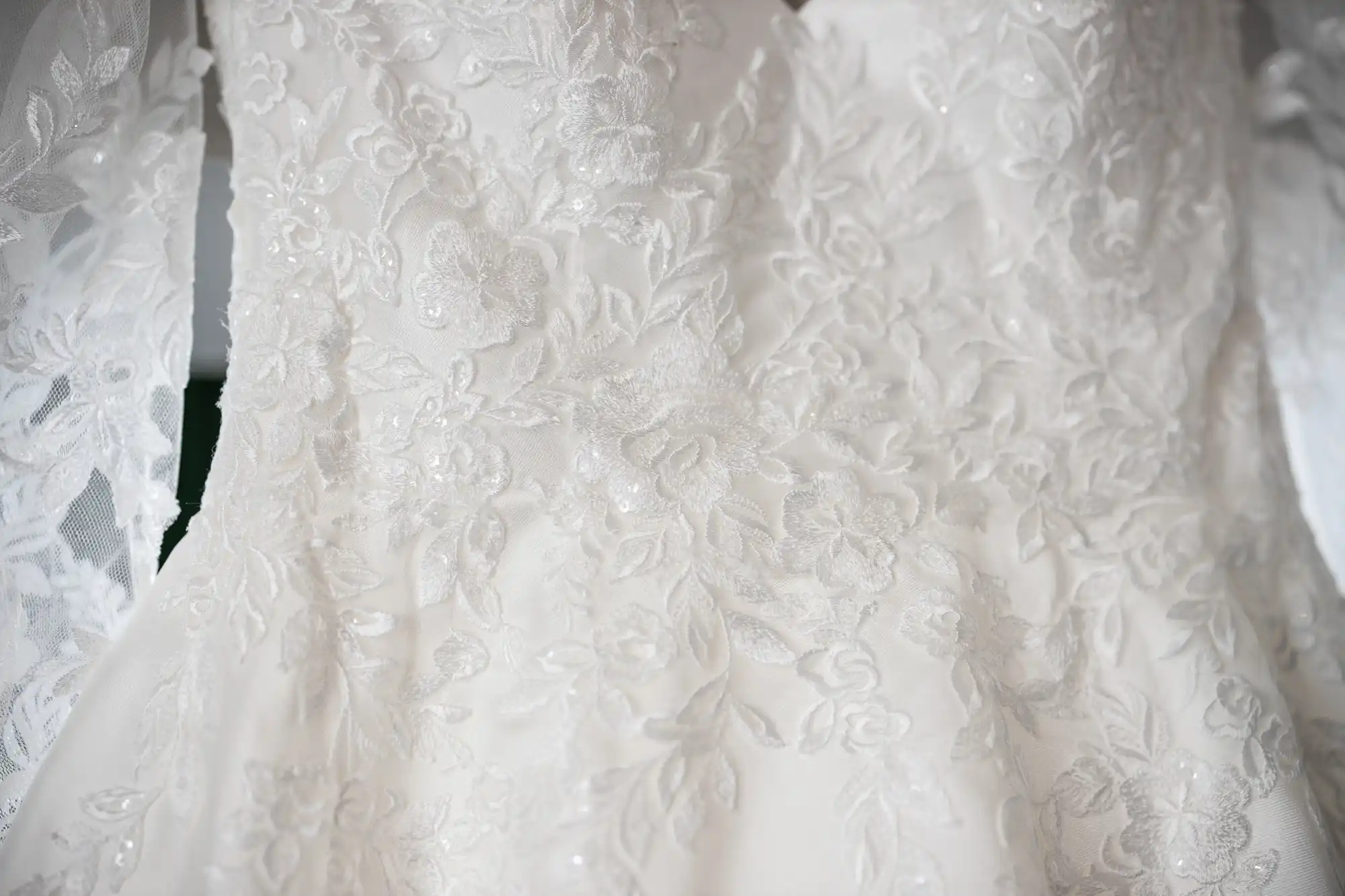 Close-up of intricate white lace on a wedding dress, featuring floral patterns and delicate detailing.