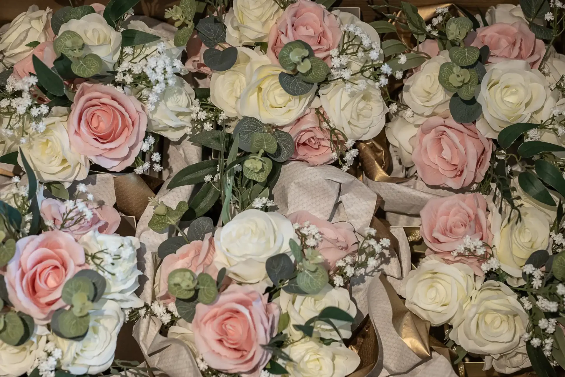 Close-up of multiple floral arrangements featuring pink and white roses, baby's breath, and eucalyptus leaves, accented with beige ribbons.