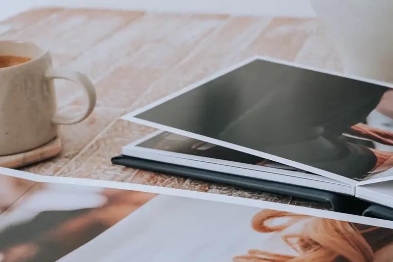 A coffee cup and a stack of open photo books with images on a wooden table.