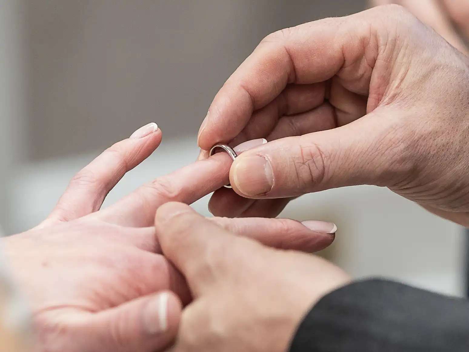 Close-up of a person placing a wedding band on another person's ring finger.