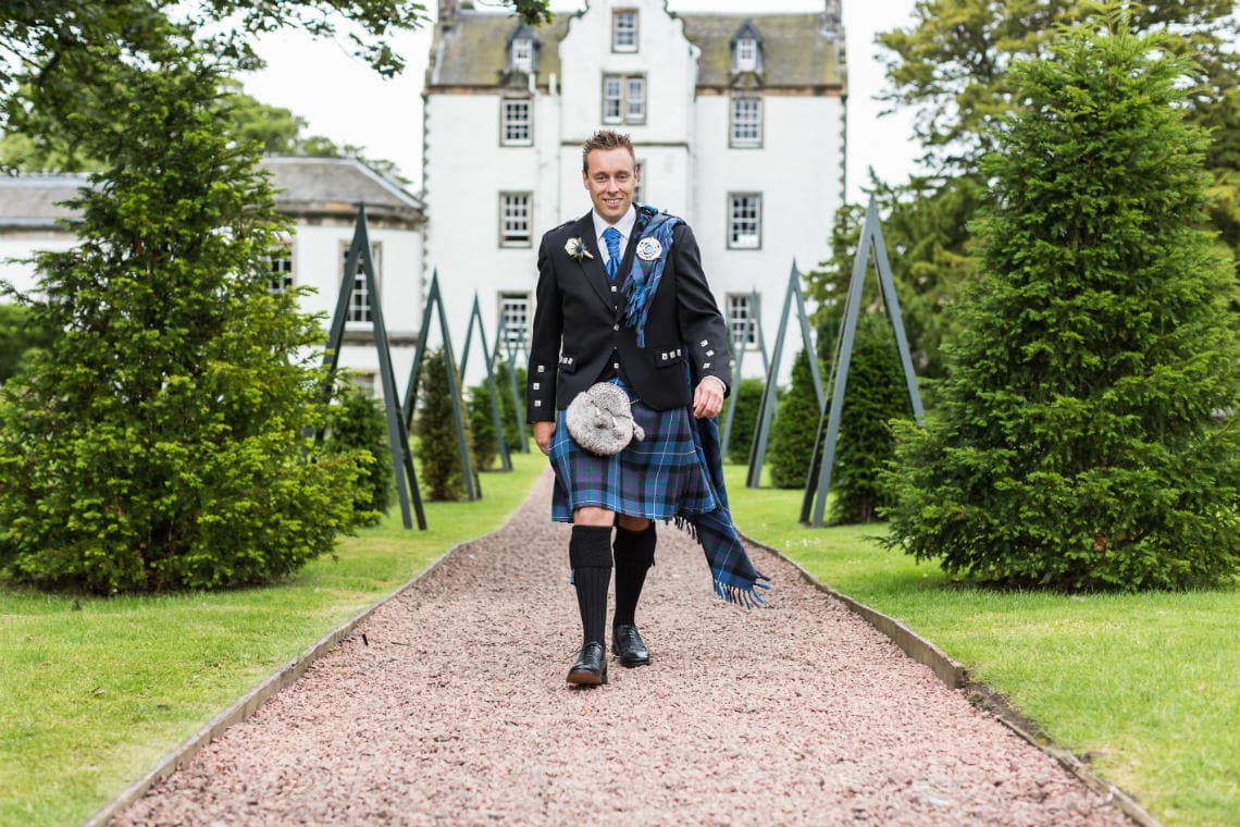 groom walking towards the camera on the gravel path in the gardens