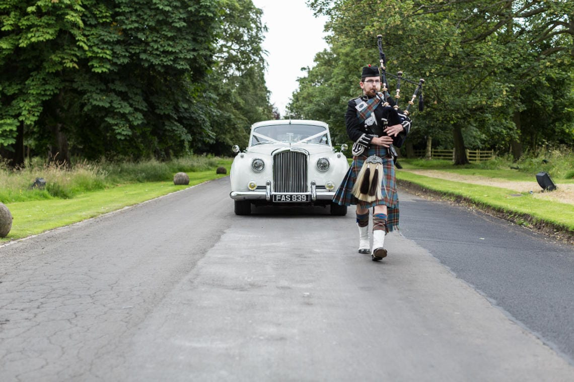 piper escorts the bride in her white Rolls Royce as she travels up the driveway
