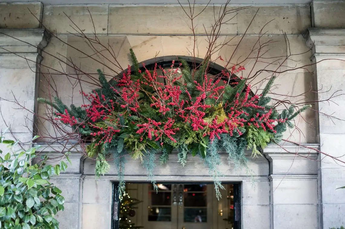 A vibrant holiday floral arrangement with red berries and greenery displayed on a stone window ledge.