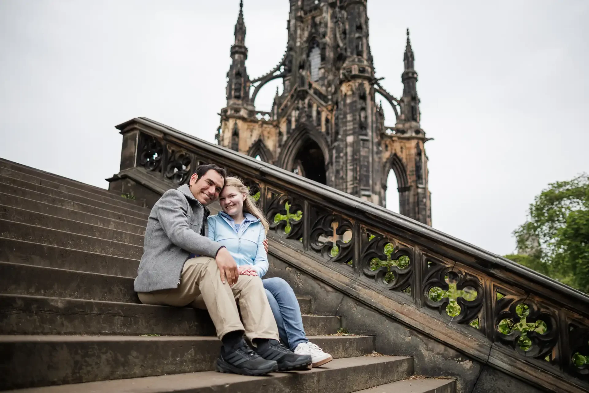 A man and woman sitting on stairs with a stone building in the background.