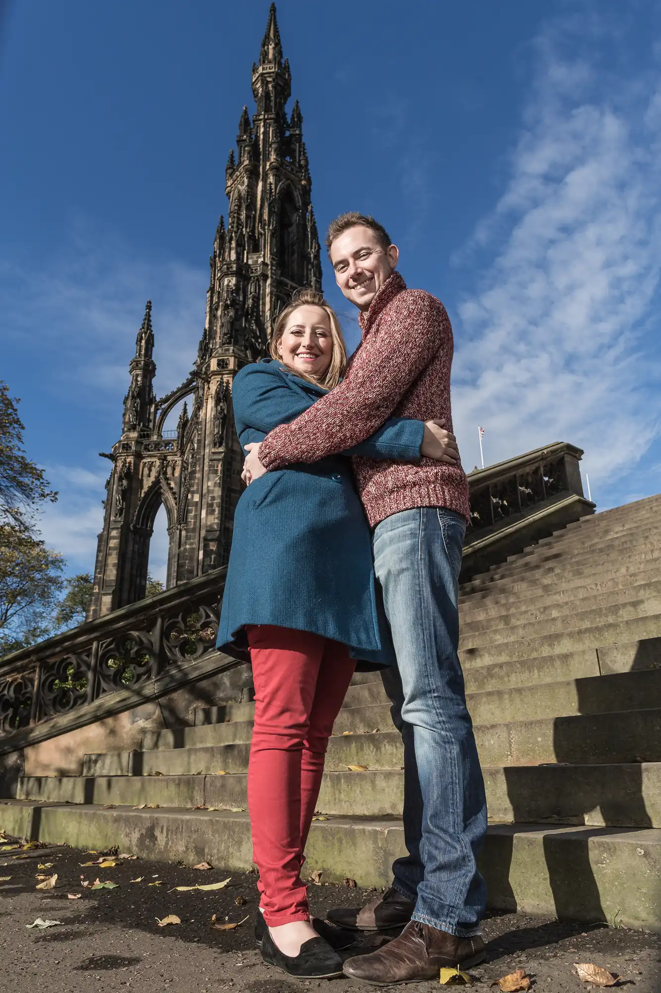 A couple embracing and smiling for the camera in front of the scott monument on a sunny day with clear blue skies.