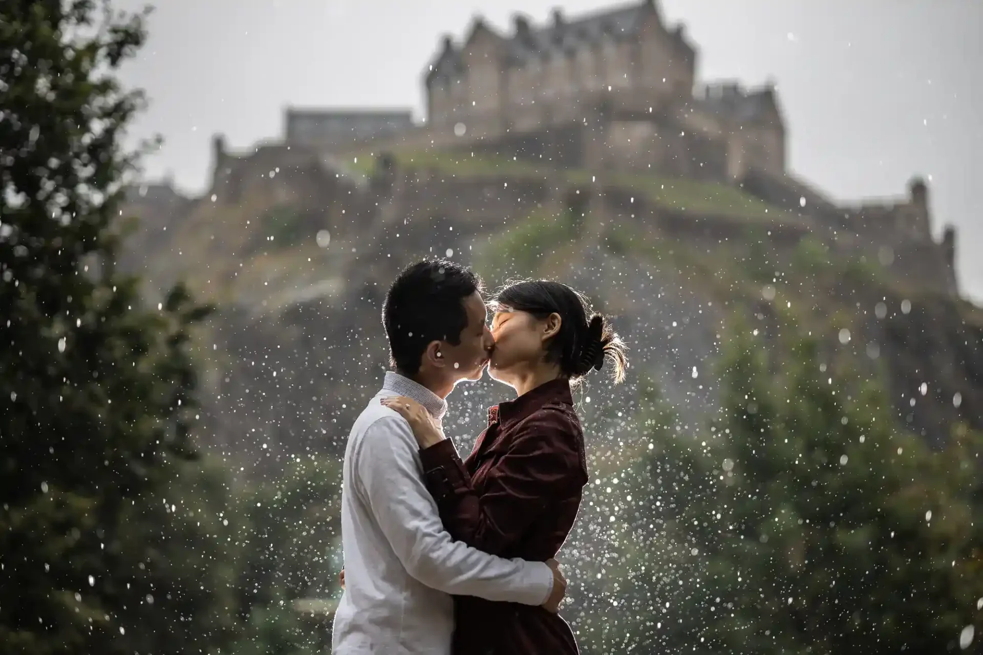 A couple kisses in the rain with a blurred castle in the background.