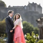 The Scotsman Hotel wedding photographer: A man and woman holding hands, smiling at each other, standing outdoors with a historic building in the background.