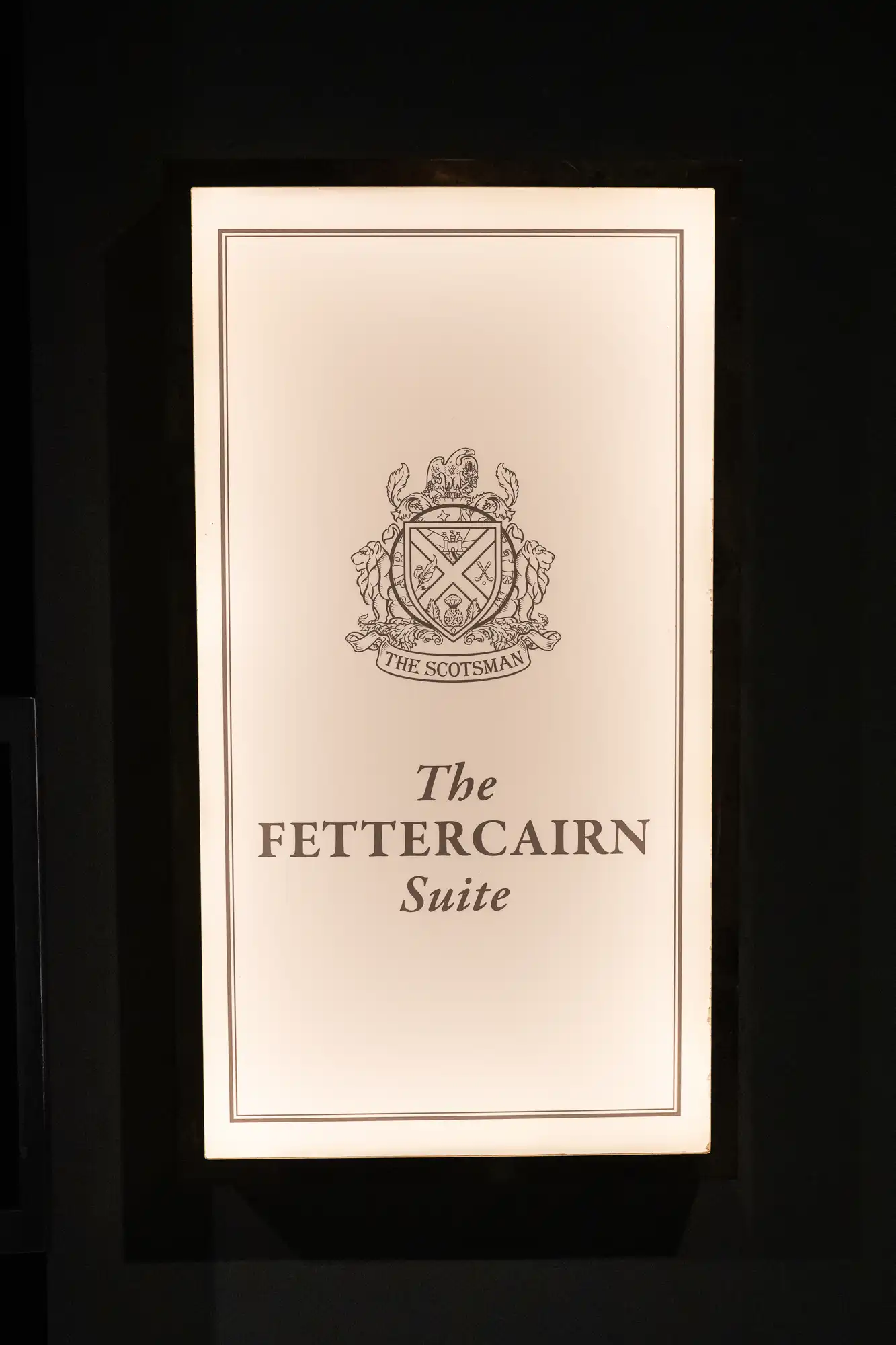 Illuminated sign with a crest and the text "The Scotsman" above "The Fettercairn Suite" on a dark background.