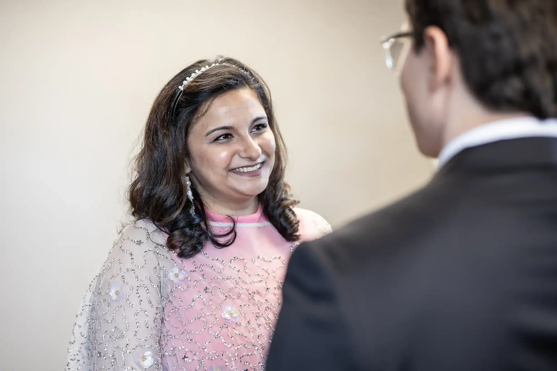 A woman in a pink dress with embroidered details smiles at a man in a suit, who is facing away.