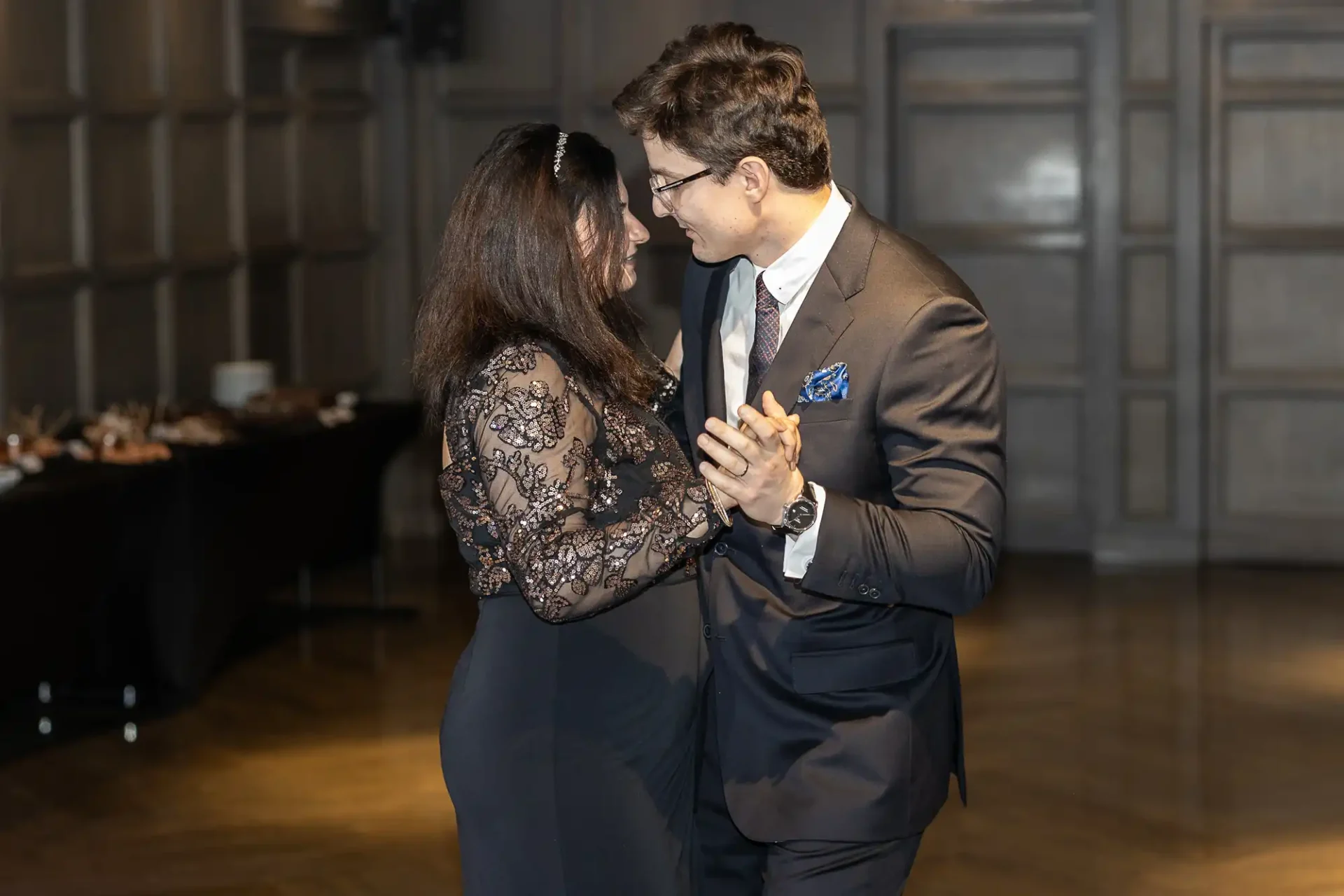 A man and woman dance together in a dimly lit room, both dressed in formal attire.