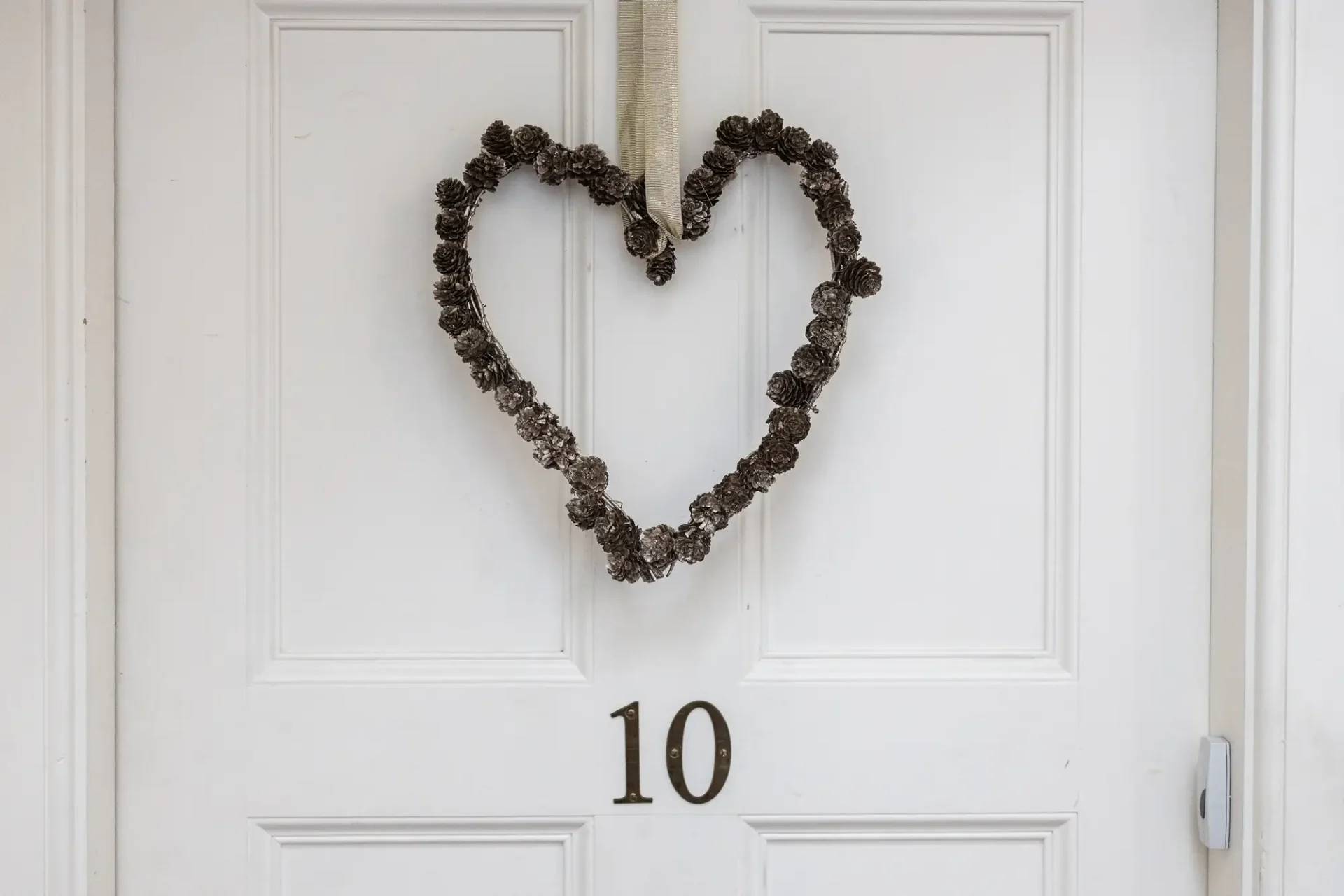 A heart-shaped wreath made of pine cones hangs on a white door with the number 10.