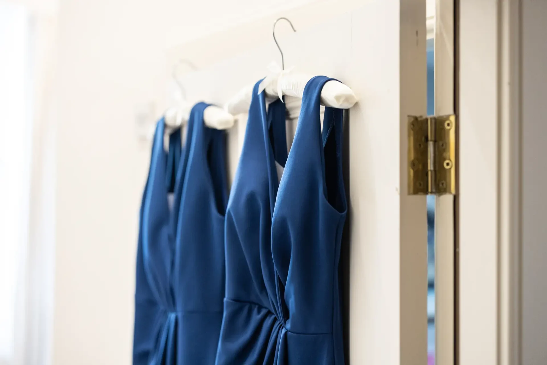 Blue dresses hanging on white hangers against a white door with a metallic lock.