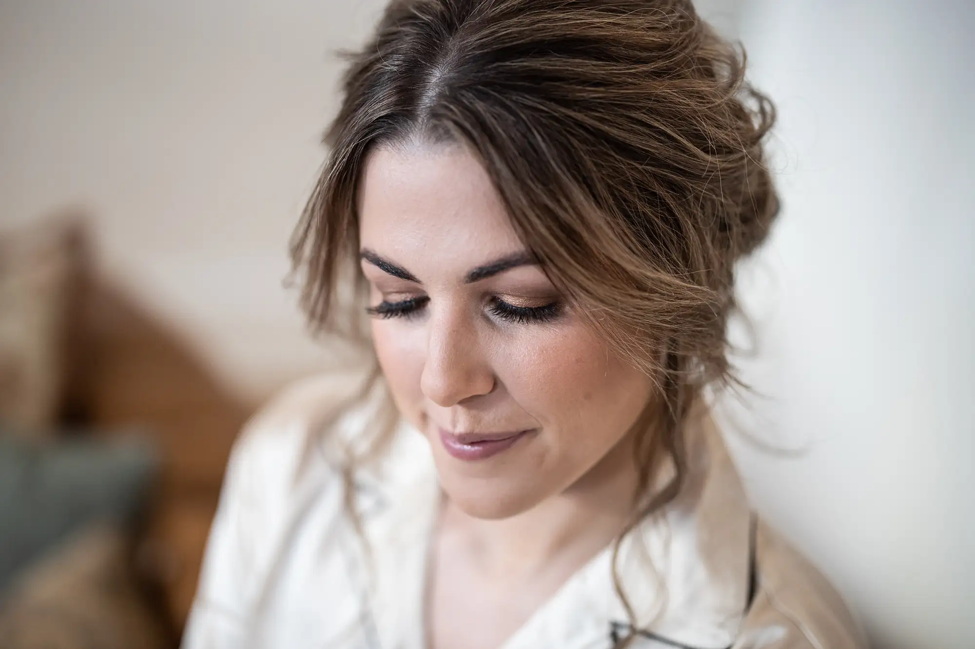 A woman with wavy brown hair, wearing a white shirt, looks down thoughtfully.