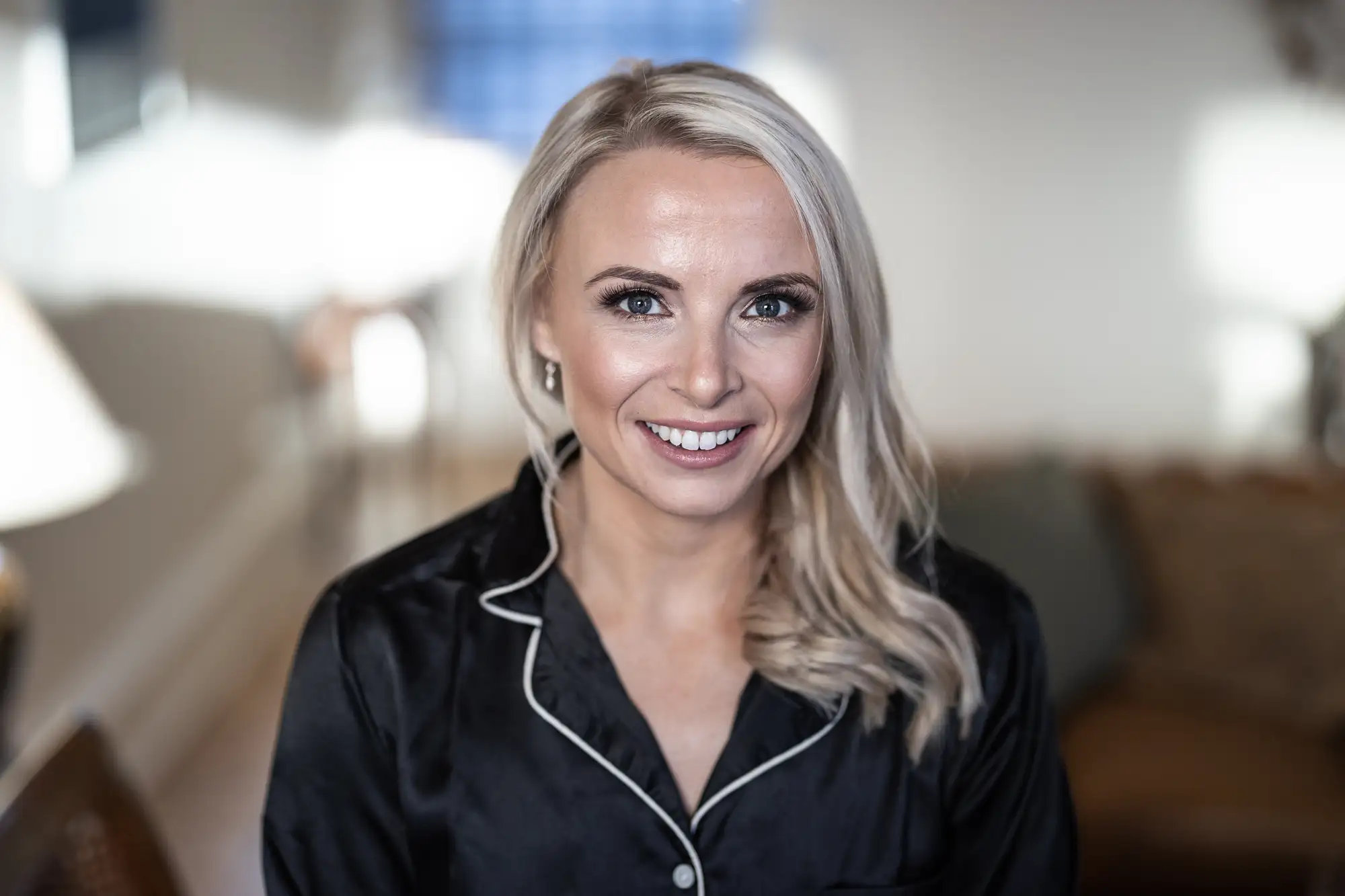 Smiling woman with blonde hair wearing a black shirt, sitting indoors with a softly blurred background.