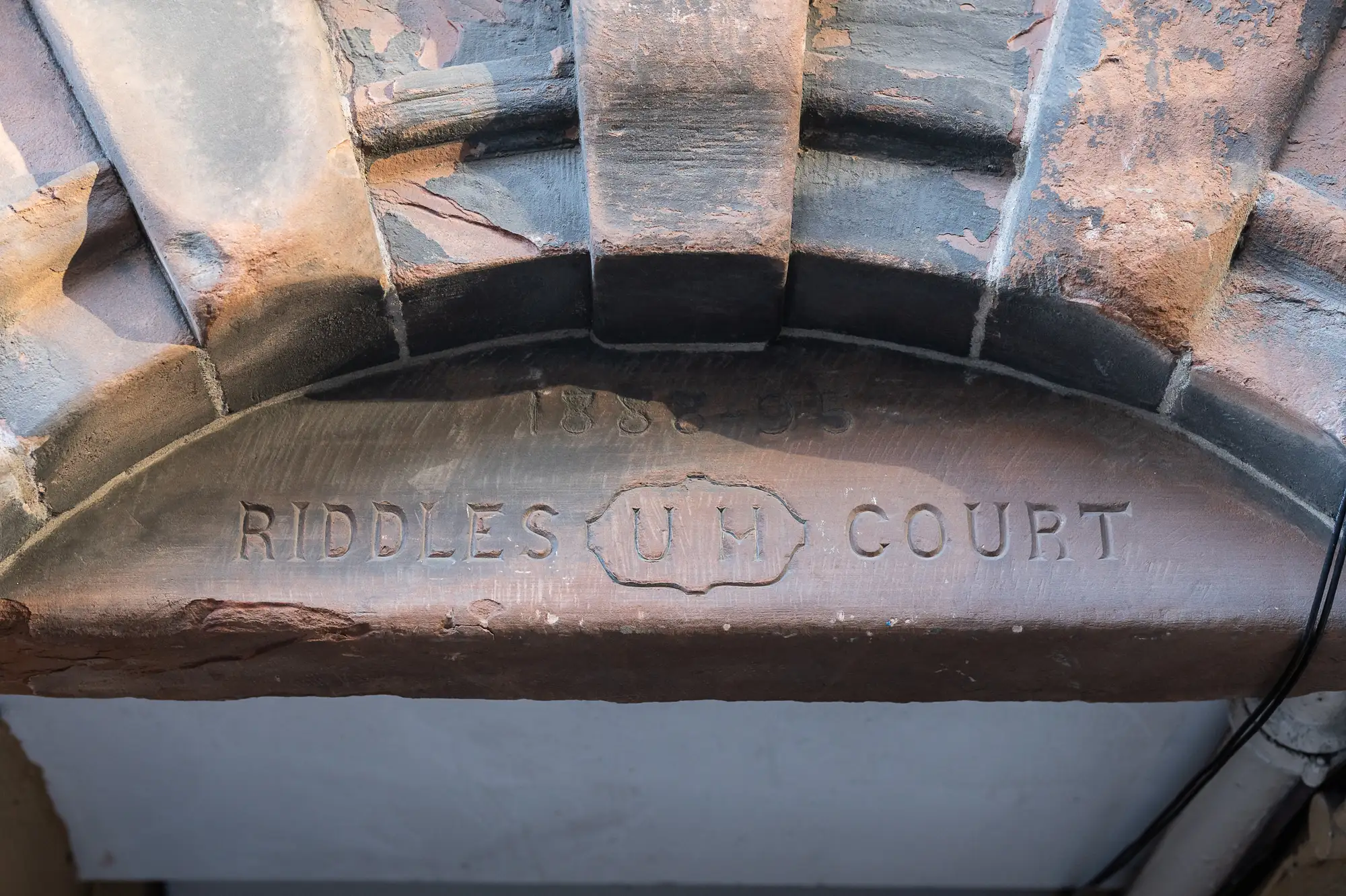 Stone archway with the inscription "riddle's court 1587-35" carved into the keystone, surrounded by aged bricks and wooden beams.