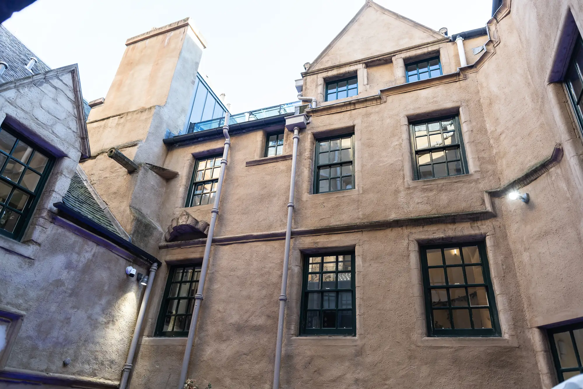 An old, narrow courtyard surrounded by high beige walls with multiple windows featuring different designs, under a clear sky.