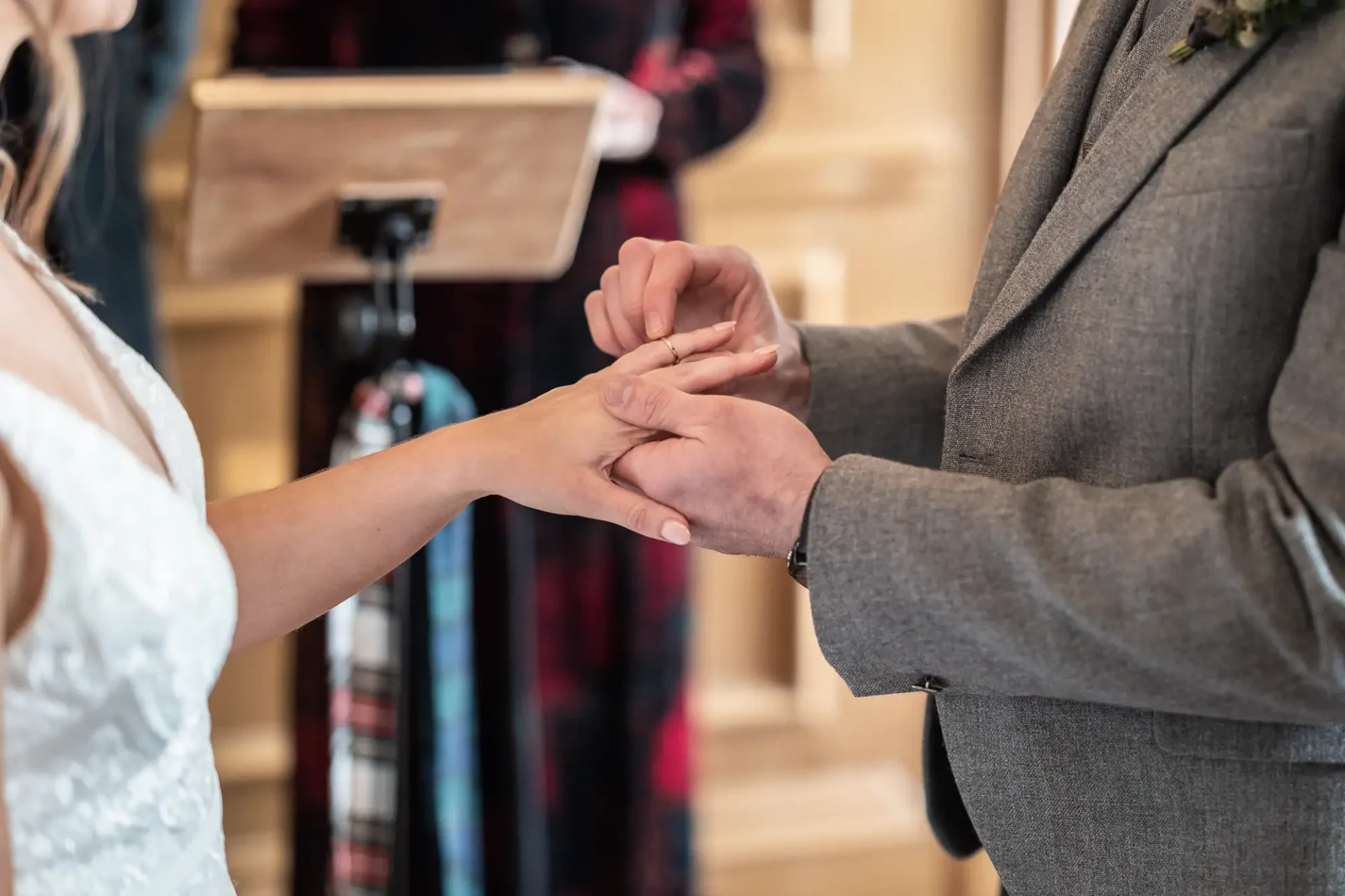 Bride and groom holding hands during a wedding ceremony, with the groom placing a ring on the bride's finger.