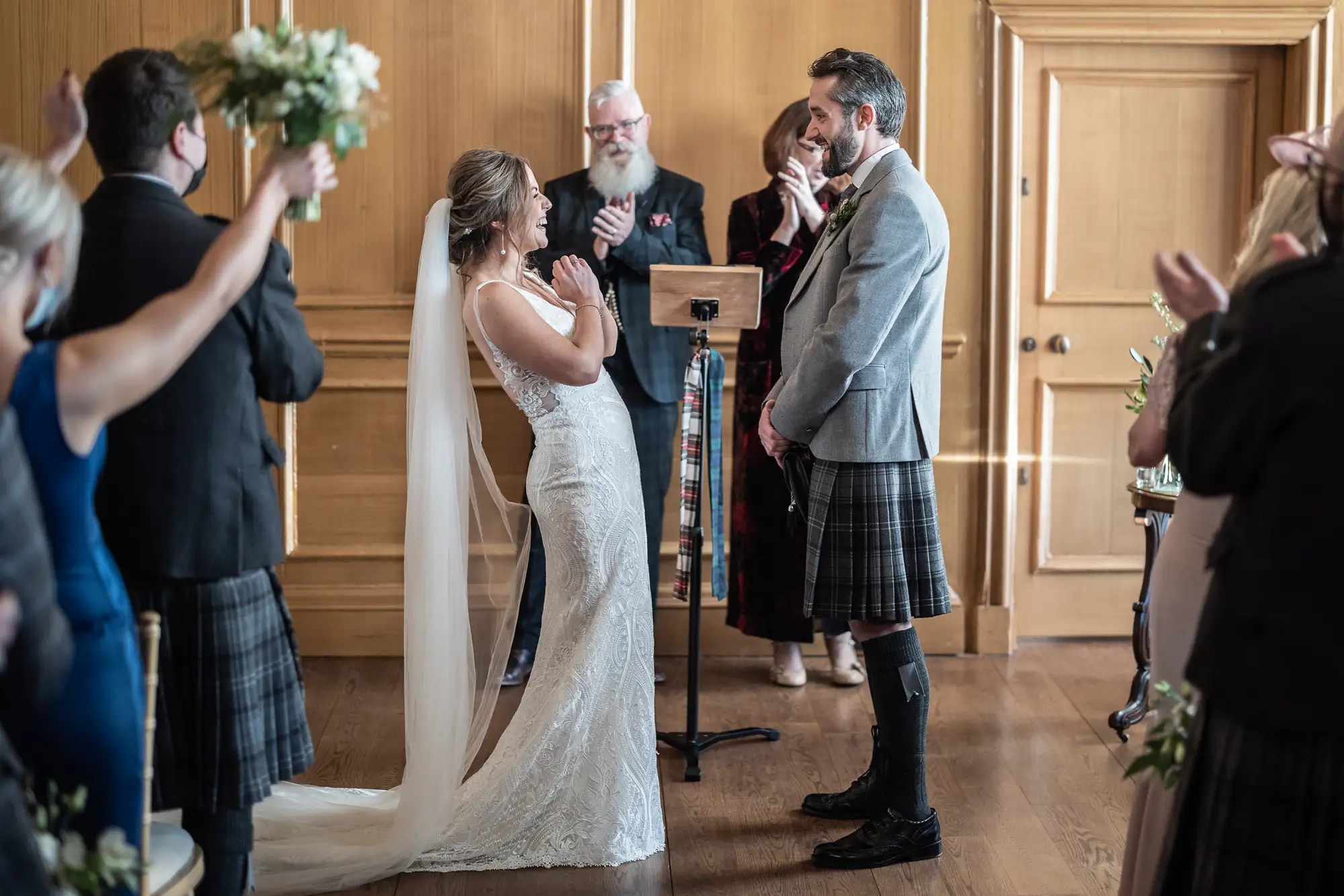 Bride and groom emotionally reacting during their wedding ceremony, with guests clapping in an elegantly decorated room.