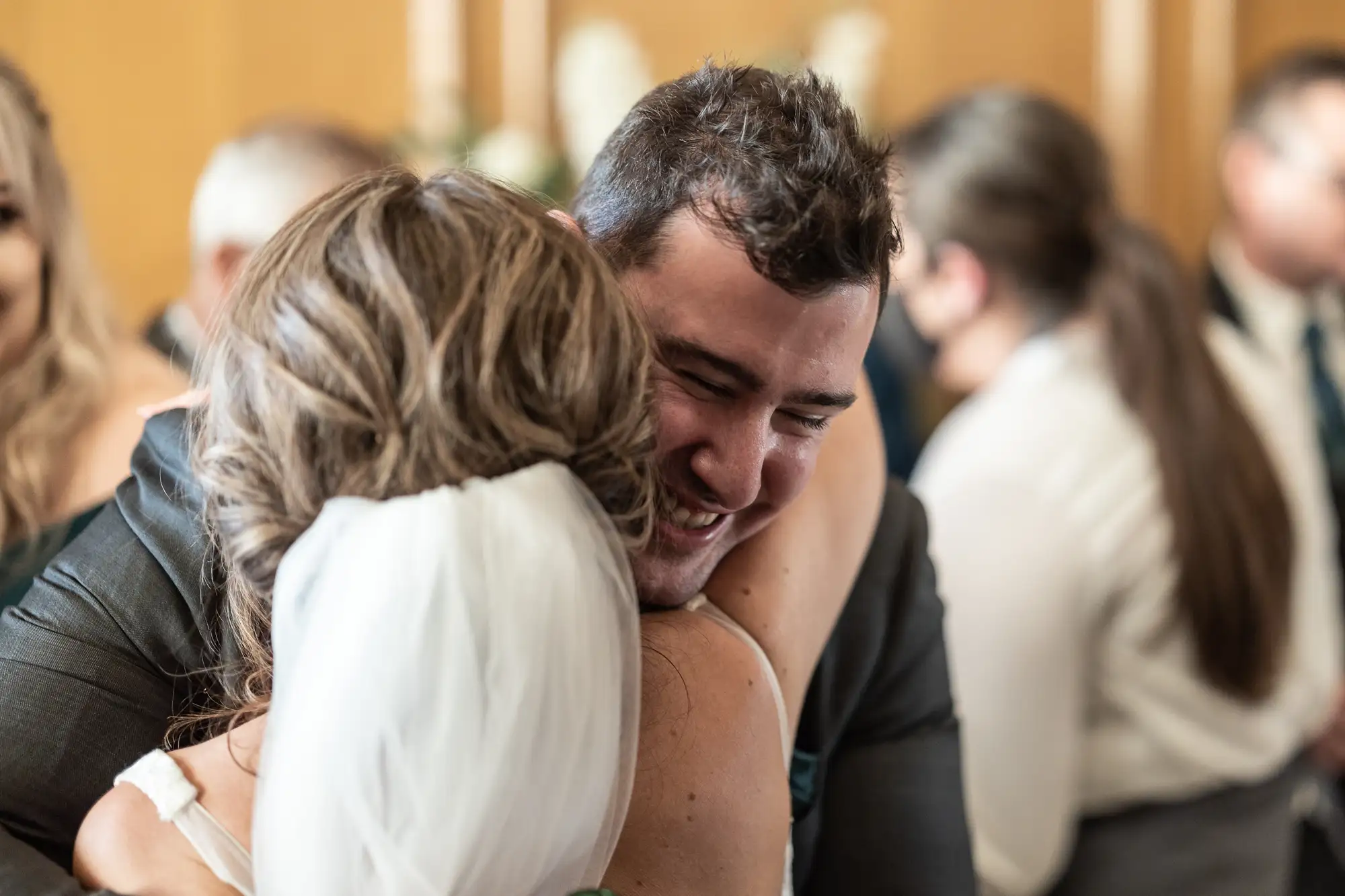 A man and woman joyfully embracing at a formal event, with guests in the background.