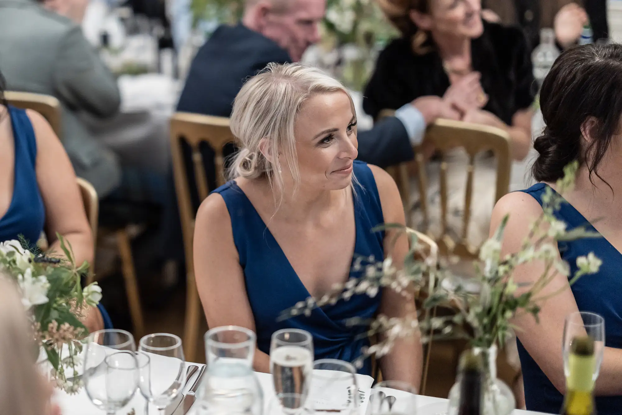 A woman in a blue dress with a thoughtful expression seated at a banquet table during a formal event.