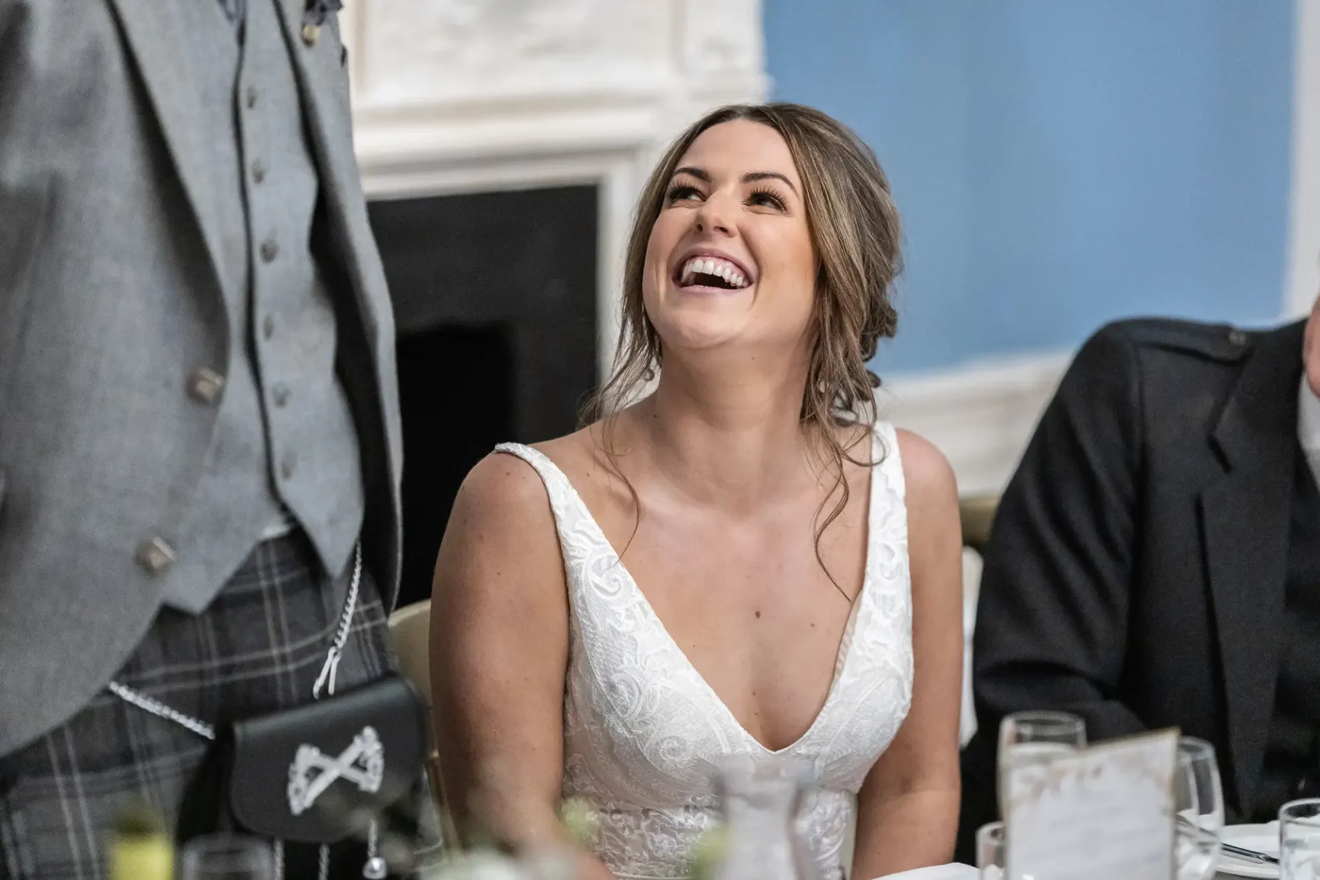A joyful bride laughing at a wedding reception, surrounded by guests in formal attire.