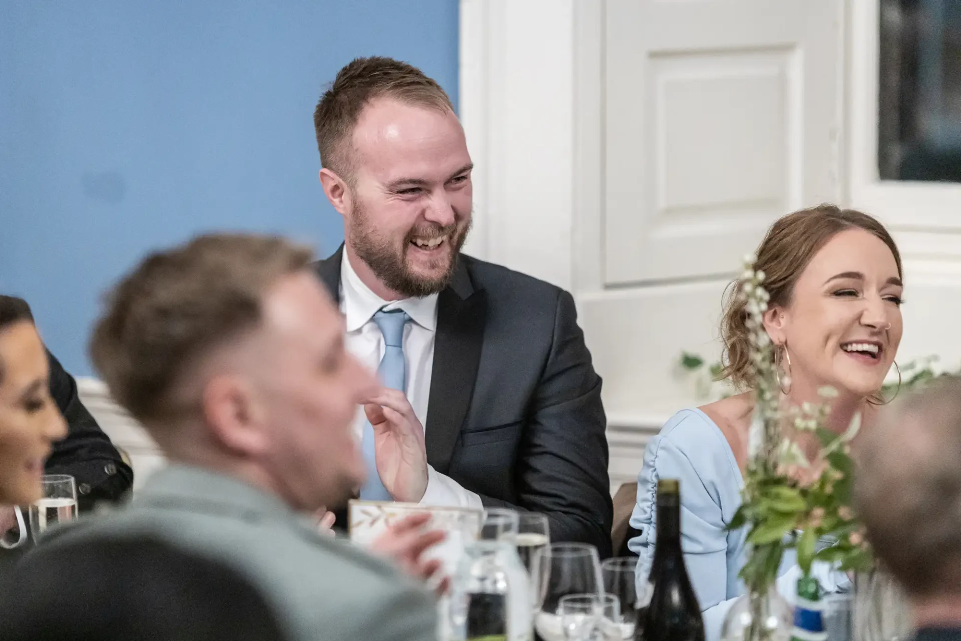 A group of people at a formal event, laughing and conversing around a dining table.